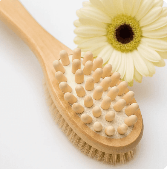 Wooden body brush with massage nodules and natural bristles next to a yellow gerbera daisy.